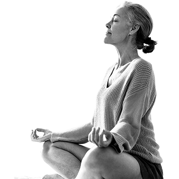 An individual looking calm sits in a yoga pose with legs crossed and hands on knees