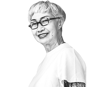 An individual with tattoos and glasses is turned sideways and smiling