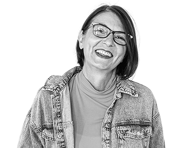 A person wearing glasses and a jean jacket tilts head and smiles